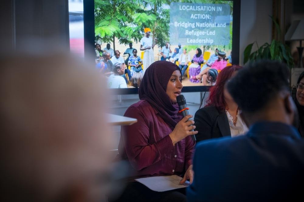 A woman in a headscarf speaks into a microphone in front of a slide reading Localisation in Action.